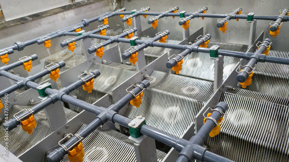 Close-up of an industrial water treatment system showing multiple rows of pipes and spray nozzles over metal filter plates inside a rectangular tank.