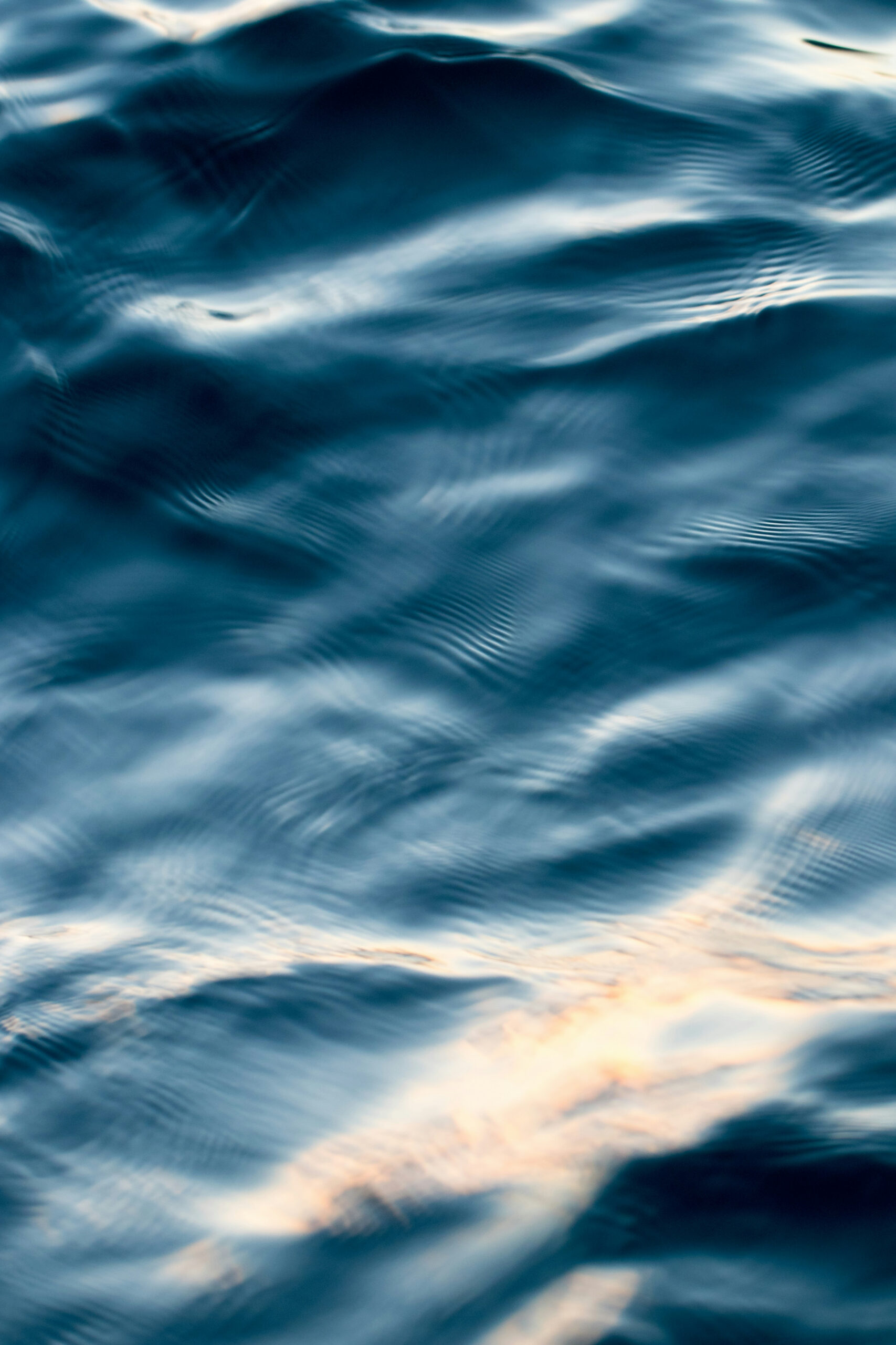 Close-up of gently rippling blue water with soft light reflections, creating a serene and abstract pattern on the surface.